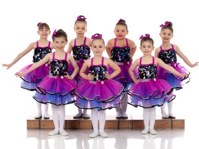 Seven young ballet dancers in purple costumes posing together.