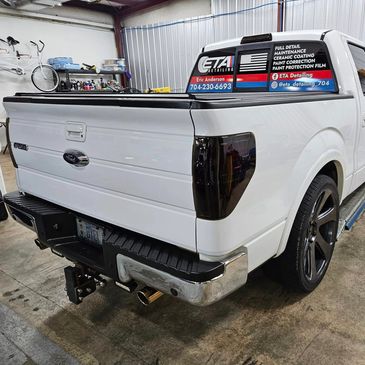 White pickup truck with tinted taillights and business advertisement window sticker.