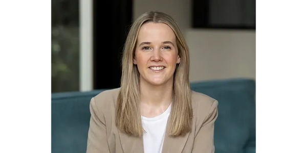 Smiling woman with long blonde hair wearing a beige blazer and white shirt.