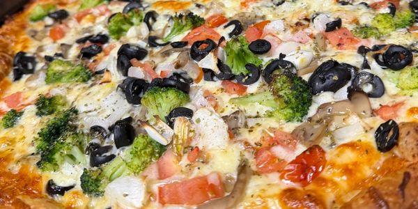 Close-up of a vegetable pizza with olives, broccoli, tomatoes, and onions.