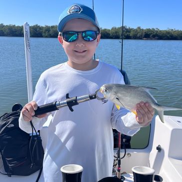 Boy in sunglasses holding a freshly caught fish on a boat.