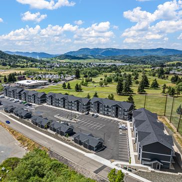 Aerial view of a modern apartment complex near green fields and mountains.