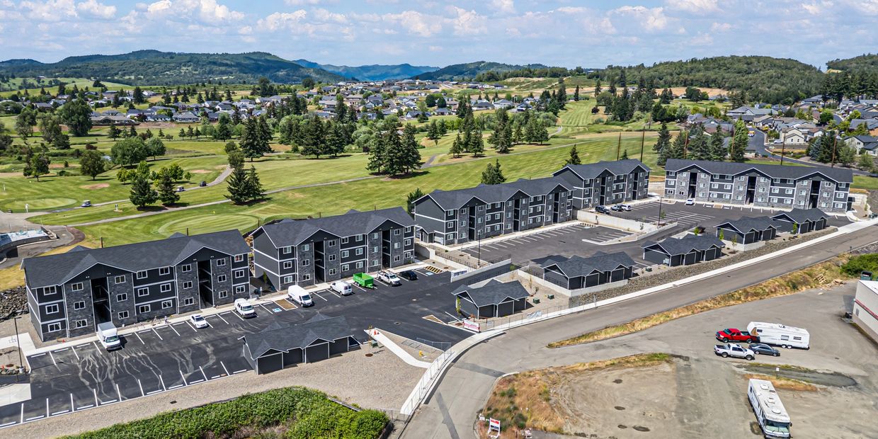 Aerial view of modern apartment buildings near a golf course with surrounding hills and residential homes.