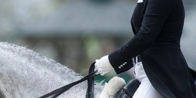 Equestrian rider in formal attire on a white horse during competition.