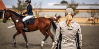 A person watches a rider on a horse in an outdoor arena.