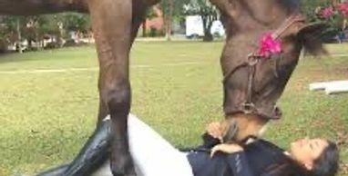 A horse nuzzles a woman lying on the grass outdoors.