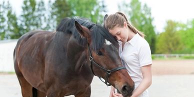 A girl gently resting her forehead against a brown horse's head outdoors.