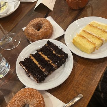 Two servings of choclate and vanilla cake. On wooden table with other desserts.