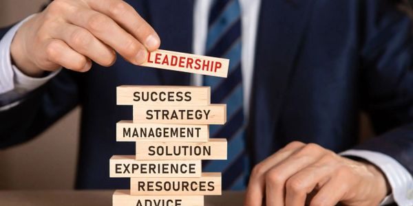 A person stacking blocks labeled with business concepts, placing 'Leadership' on top.