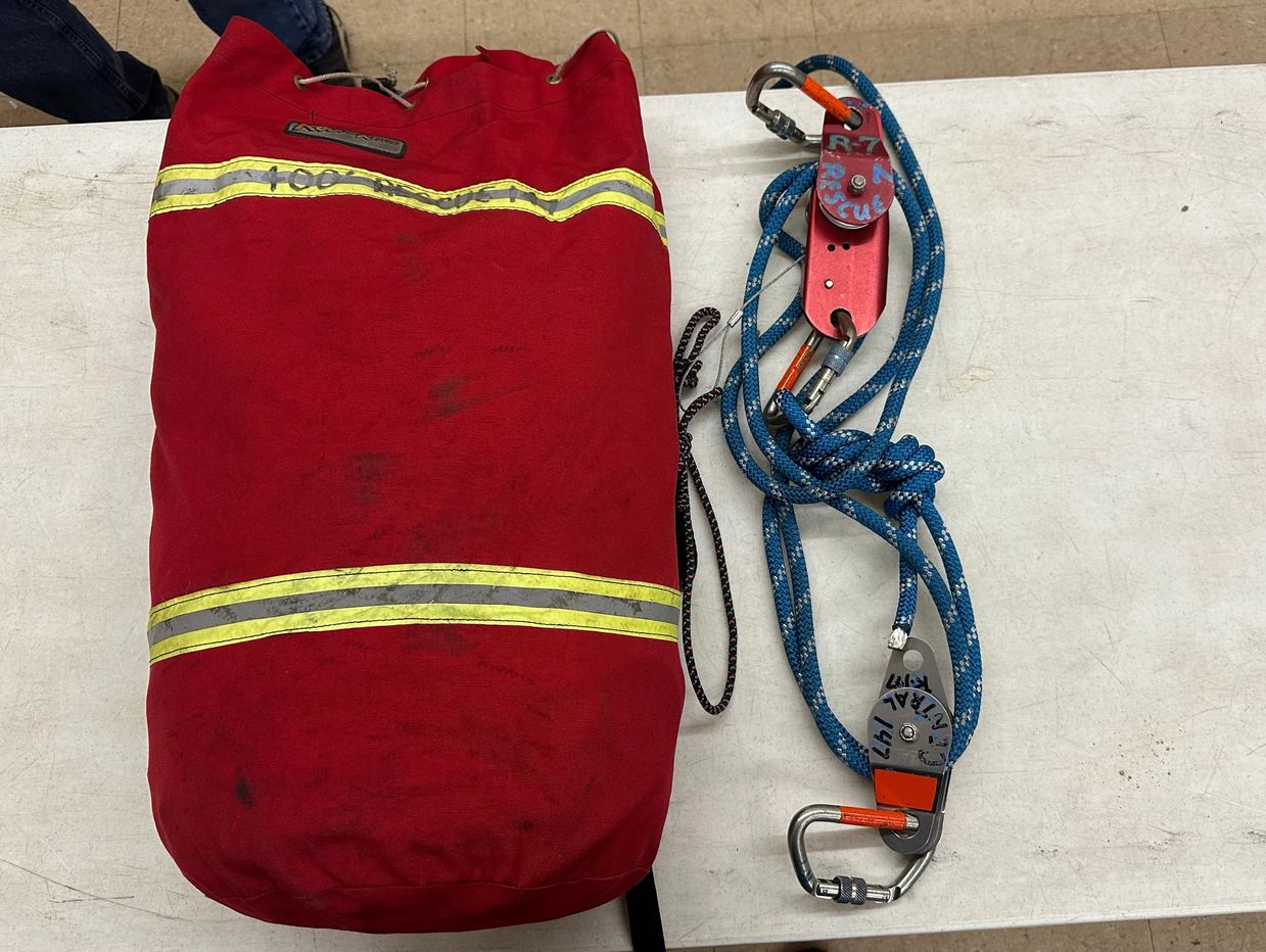 Red rescue bag and blue rope with pulleys on a white table.