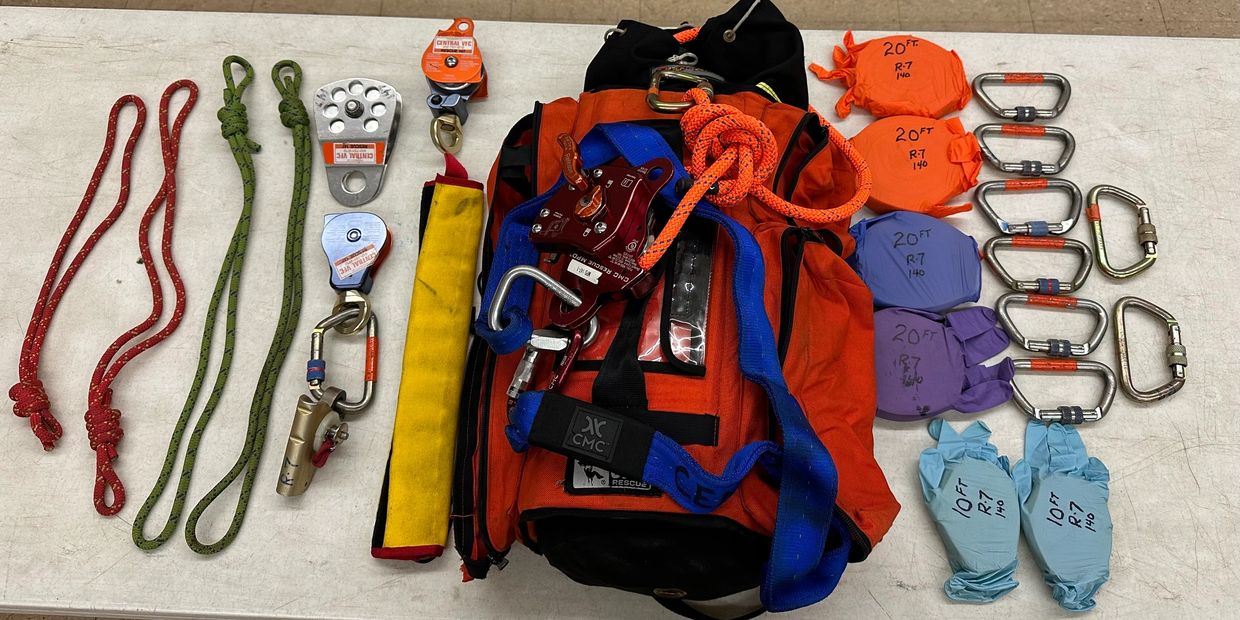 Rescue climbing gear including ropes, carabiners, pulleys, and gloves laid out on a table.