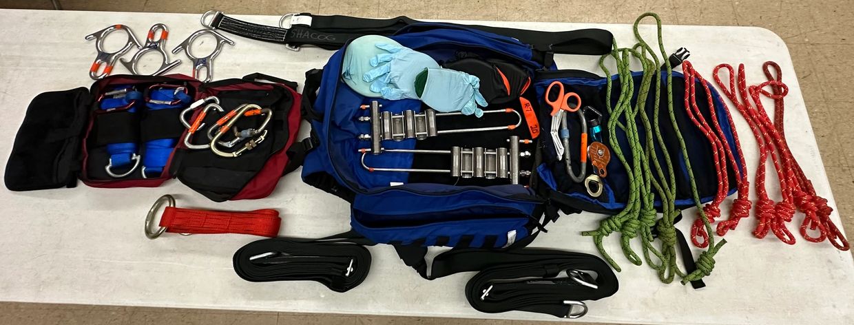 Climbing and rescue gear laid out on a table including ropes, carabiners, and gloves.
