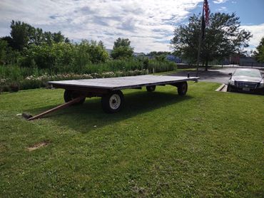 A flatbed trailer parked on a grassy area near a car and flagpole.