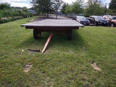 Flatbed trailer parked on grass near cars and trees.