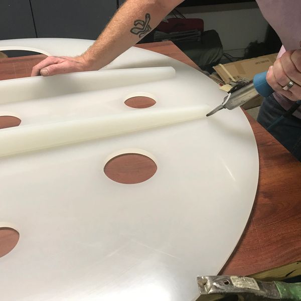 Person using a heat gun on a white plastic sheet with circular cutouts.