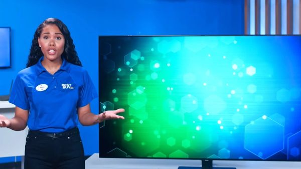 A woman in a Best Buy uniform stands next to a large screen with a blue and green digital background.