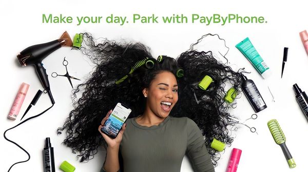 Woman smiling with phone surrounded by hair care tools, promoting PayByPhone parking.