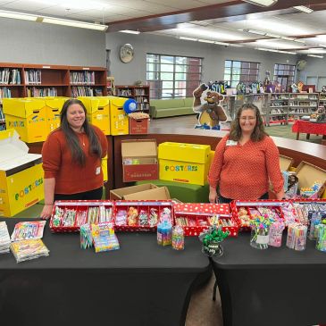 Two women standing behind a table with Christmas treats in a library.