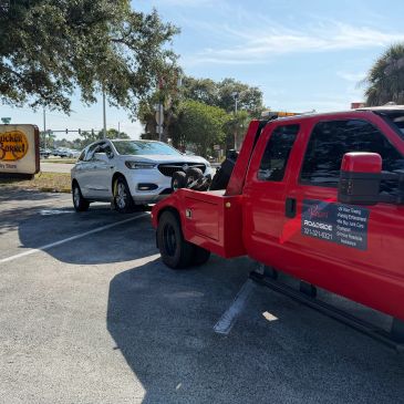 Red tow truck towing a white car in a parking lot.