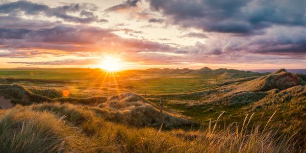 A breathtaking sunset, behind a green field that is bordering a cliff that drops off into the sea.