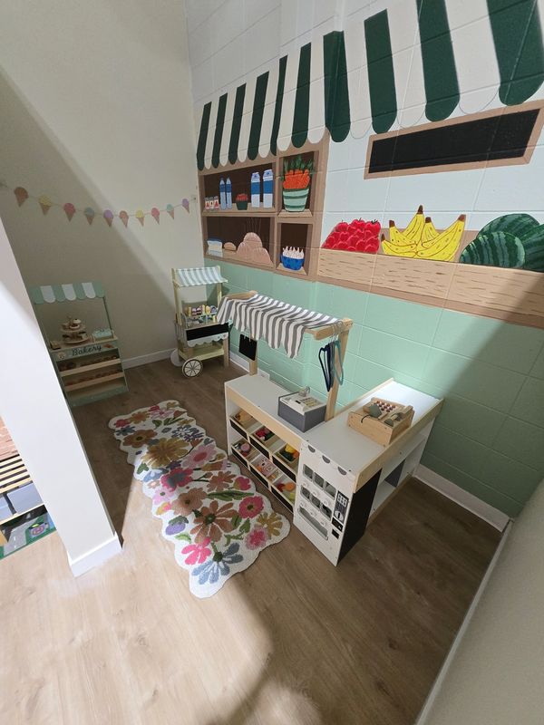 A children's play market area with wooden play stands and colorful wall mural.