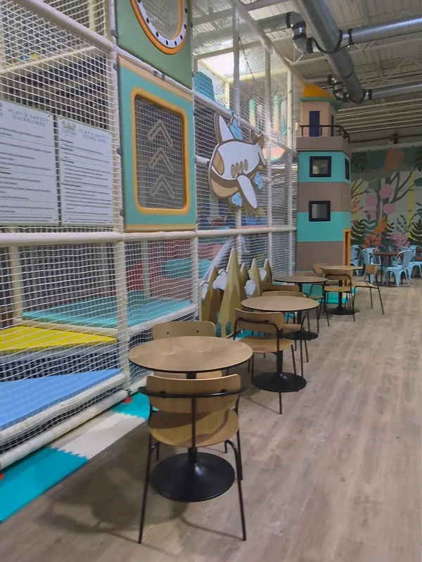 Indoor play area with tables and chairs alongside a colorful soft play structure.