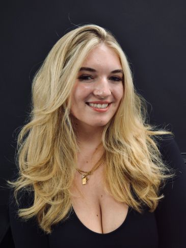 Blonde woman with long hair smiling against a black background.