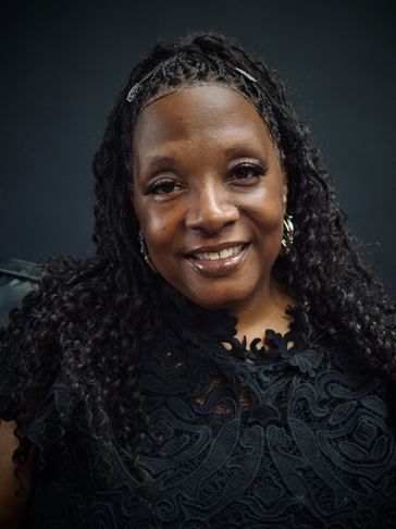 Smiling woman with curly hair wearing a black lace top.