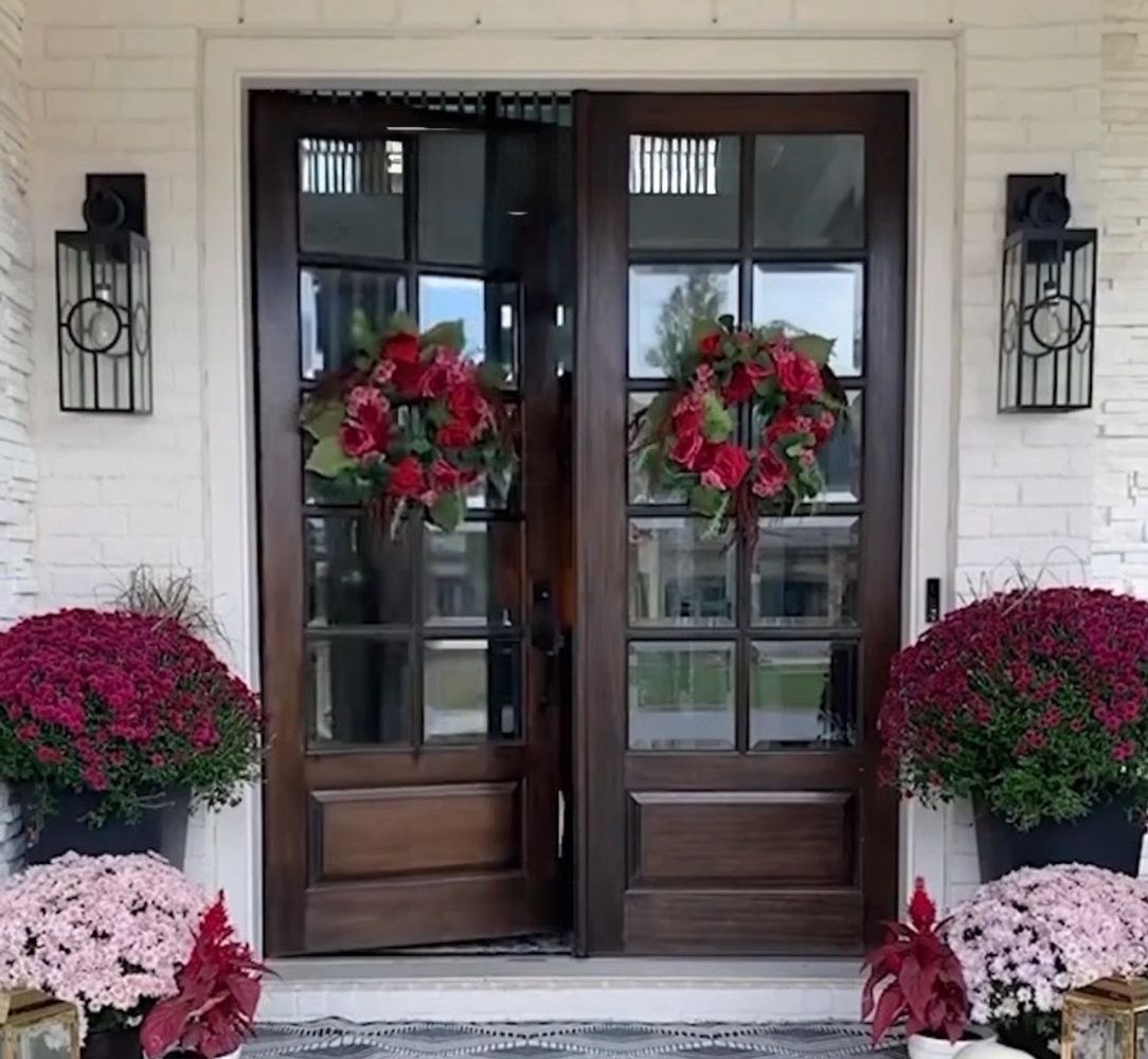 Painted white brick home with dark wooden front doors and pink and purple potted flowers.
