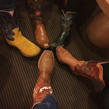 Five pairs of colorful cowboy boots arranged in a circle on a carpet.