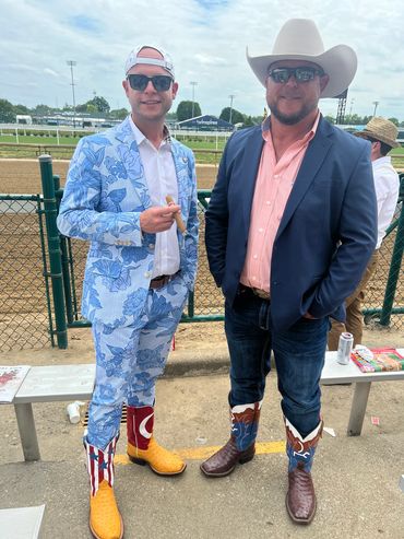 Two men in stylish suits and cowboy boots at a race track.