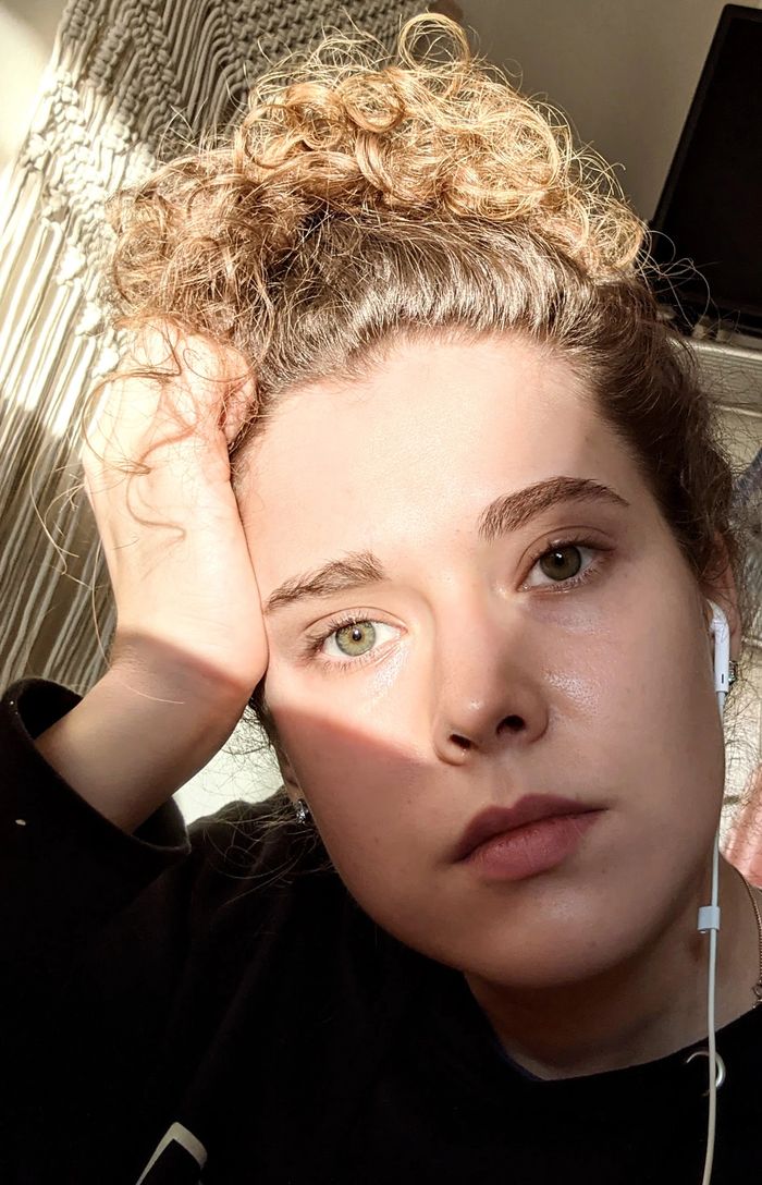 Young woman with curly hair resting her head, listening to music, bathed in warm sunlight.