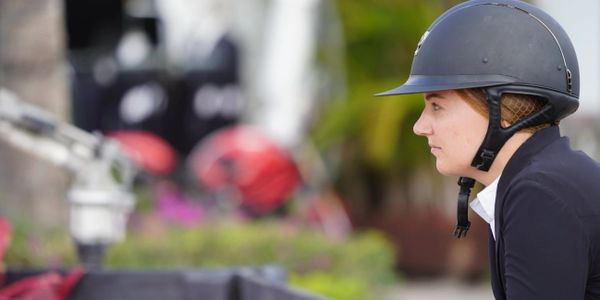 A person wearing an equestrian helmet looking focused.