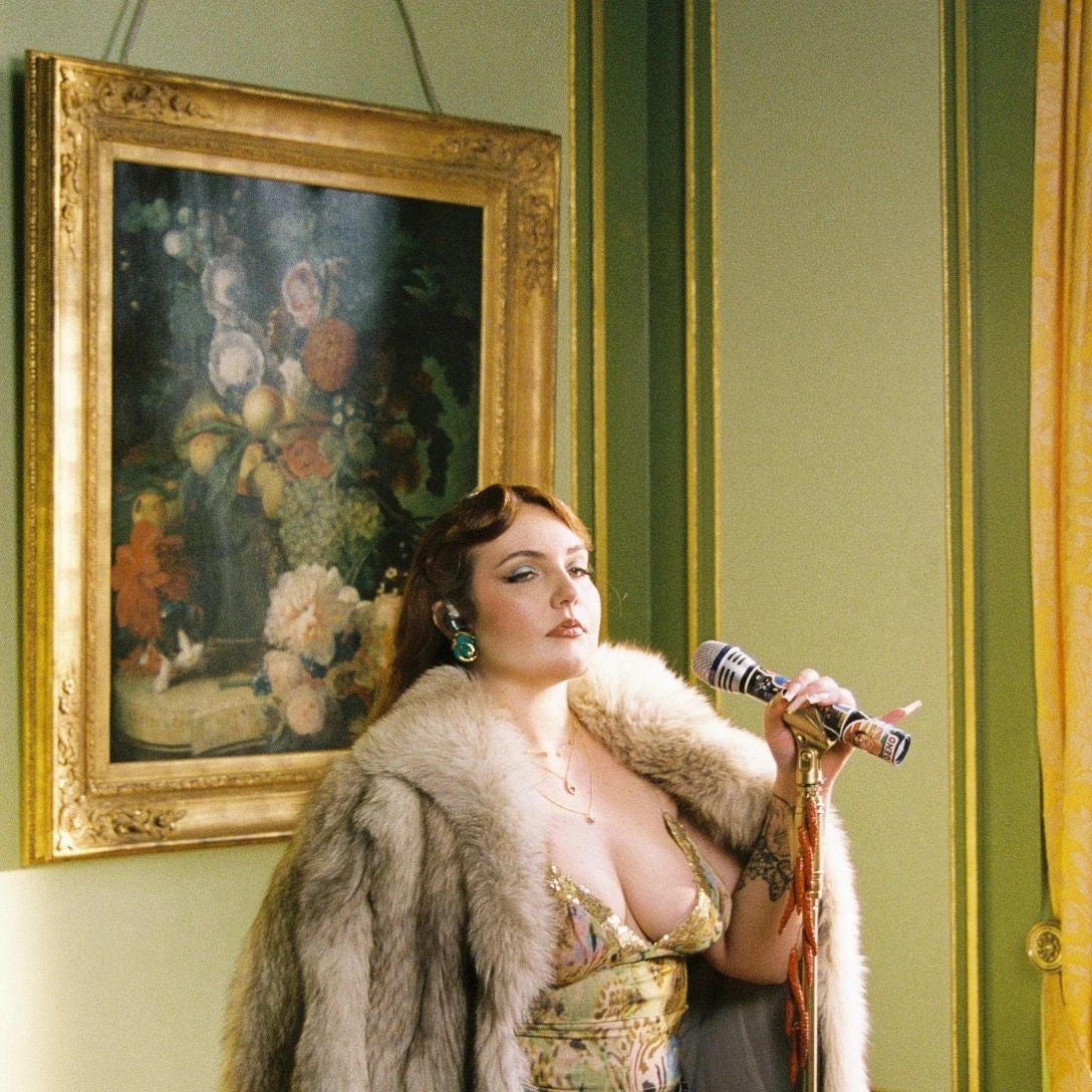 Woman in luxurious fur coat holding a microphone in an elegant room.