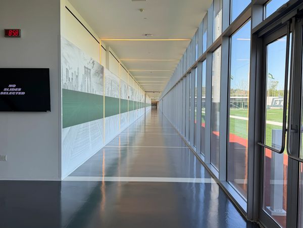 Long, modern hallway with large windows overlooking a sports field.