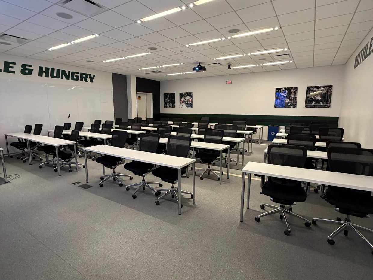 Empty modern classroom with rows of white desks and black chairs.
