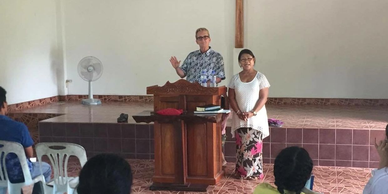 A man and woman speaking in a church with a wooden cross behind them.