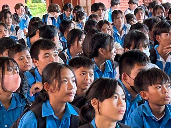 Students in blue uniforms attentively listening in a classroom setting.