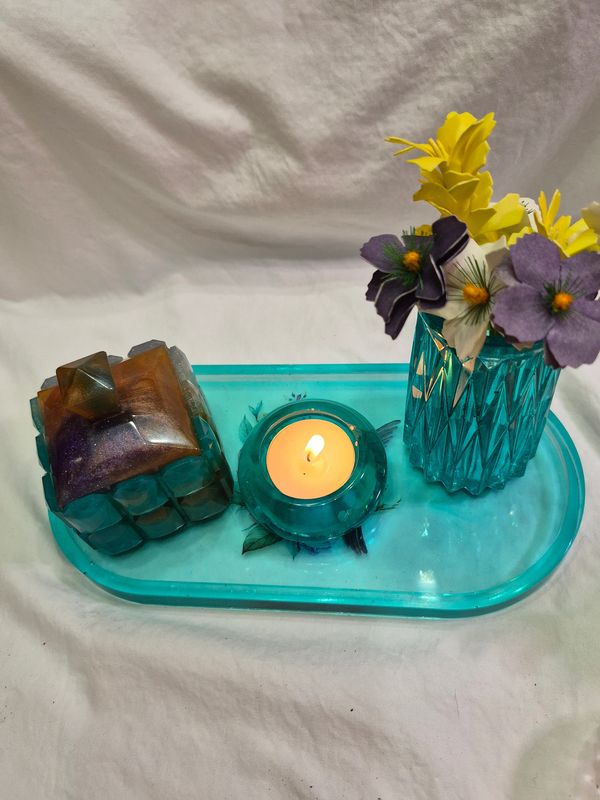 A teal tray with a candle, decorative box, and a vase of colorful artificial flowers.
