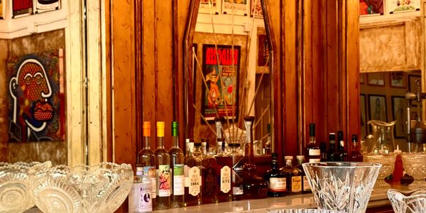 A stylish bar setup with various liquor bottles and glassware against a wooden and mirrored background.