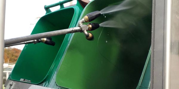Automated system spraying inside green bins for cleaning.