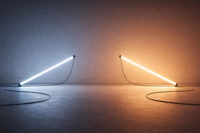 Two neon tube lights, one blue and one orange, angled on a floor with cables.