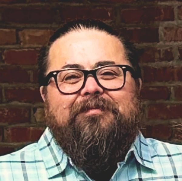 Person wearing glasses with a beard and slicked back hair.