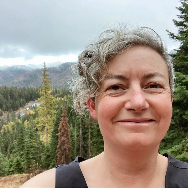 Person smiling. In the background you can see some trees and mountains.