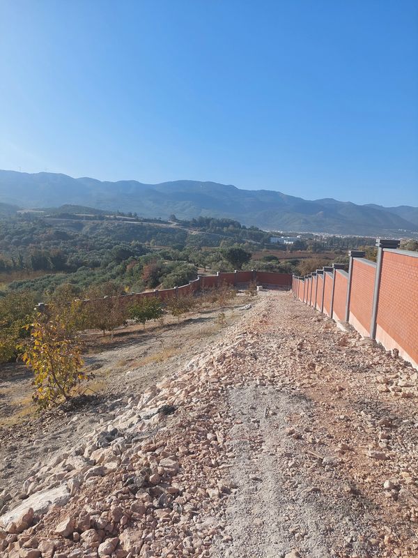 Çakıllı patika ve kırmızı tuğla duvarlarla doğal manzara.