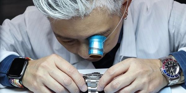 Watchmaker inspecting a wristwatch with a magnifier.