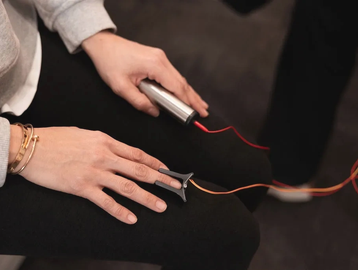 Person holding a pulse oximeter and a device connected by wires.
