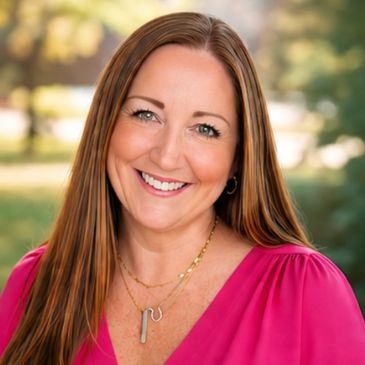 Smiling woman with long hair wearing a pink blouse outdoors.