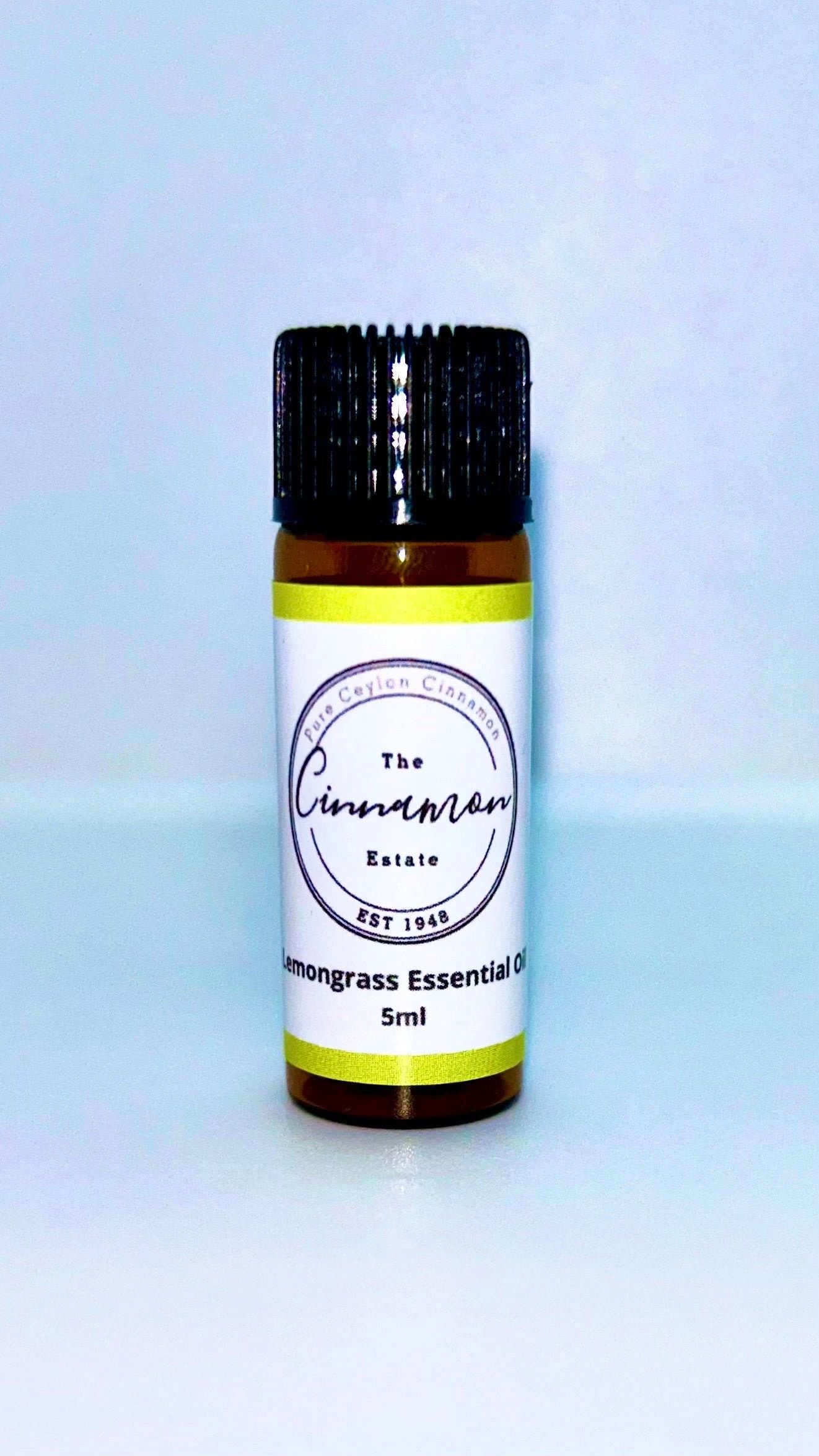 An amber dropper bottle of The Cinnamon Estate lemongrass essential oil, with a chartreuse striped label.