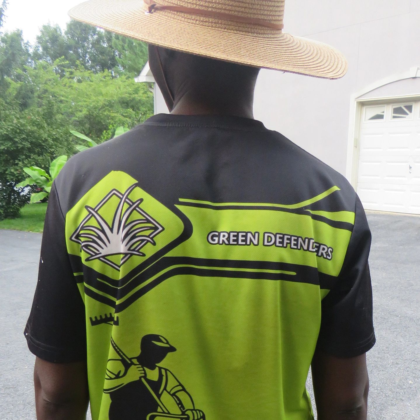 Person wearing a Green Defenders shirt and straw hat outdoors.
